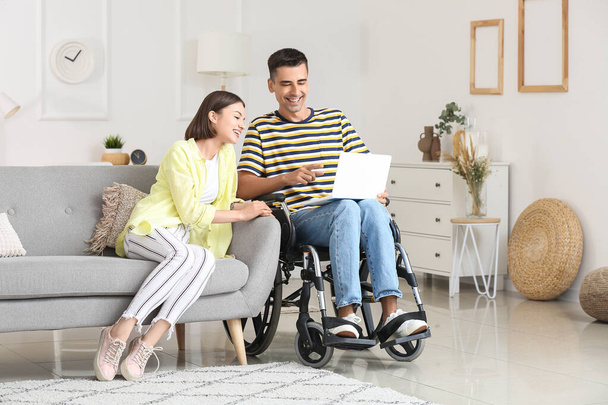 Молодий чоловік у інвалідному візку та його дружина використовують ноутбук вдома
 - Фото, зображення
