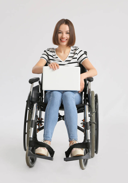 Young woman in wheelchair using laptop on light background - Fotoğraf, Görsel