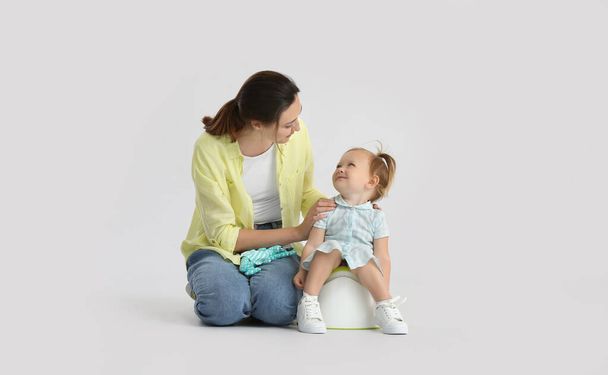 Mother potty training her little daughter on light background - Photo, Image