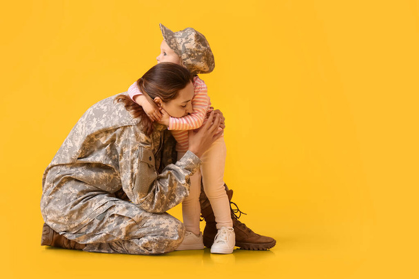 Female soldier with her little daughter on color background - 写真・画像