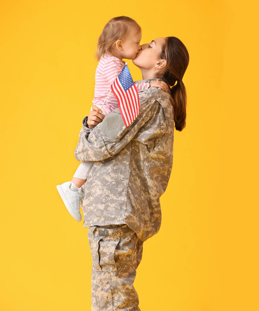 Female soldier and her little daughter with USA flag on color background - Photo, Image