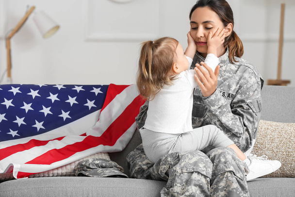 Γυναίκα στρατιώτης του στρατού των ΗΠΑ με τη μικρή κόρη της κάθεται στον καναπέ στο σπίτι - Φωτογραφία, εικόνα