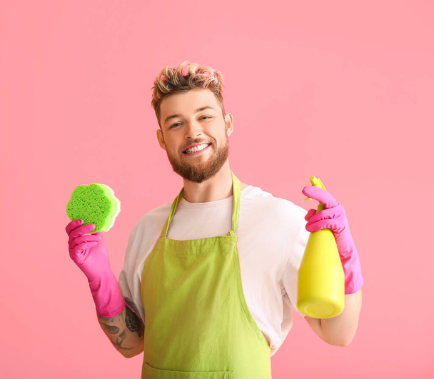 Joven guapo con esponja limpiadora y detergente sobre fondo rosa - Foto, imagen