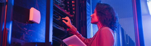 engineer holding digital tablet while checking server in data center in neon light, banner - 写真・画像