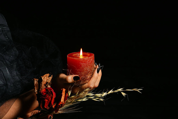 Hexe mit getrockneten Blumen und brennender Kerze für das Ritual auf schwarzem Hintergrund - Foto, Bild