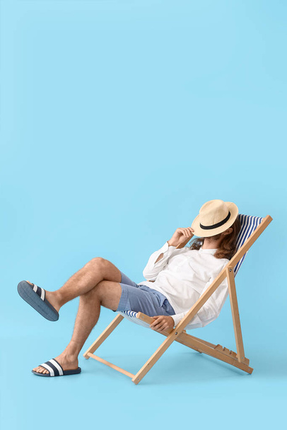 Handsome young man sitting on deck chair against color background - Фото, изображение