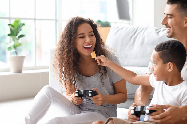 Щаслива міжрасова сім'я грає в відеогру і їсть фішки вдома
 - Фото, зображення