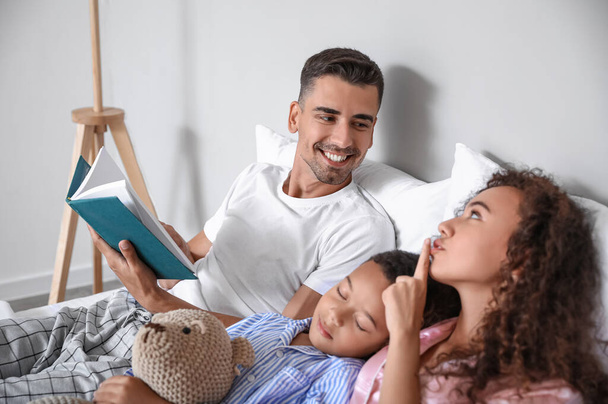 Happy interracial family reading book in bed - Foto, imagen