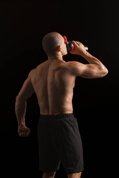 man bodybuilder drinken eiwit schudden op donkere achtergrond - Foto, afbeelding