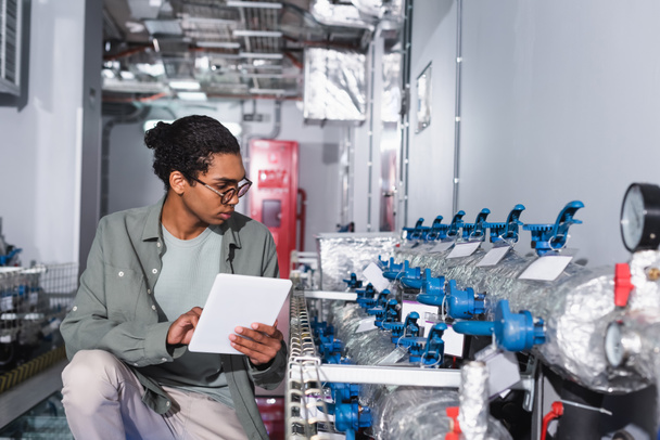 Dijital tabletli genç Afrikalı Amerikalı teknisyen veri merkezinin soğutma sistemine bakıyor. - Fotoğraf, Görsel