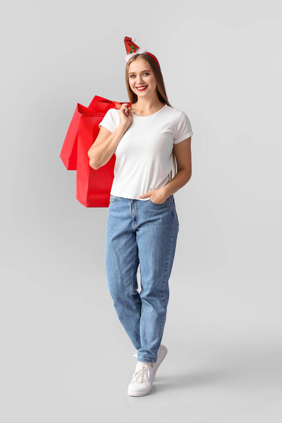 Beautiful young woman with Christmas decor and shopping bags on grey background - Fotó, kép