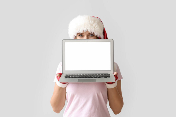 Hermosa joven en Santa sombrero y con portátil sobre fondo gris - Foto, imagen