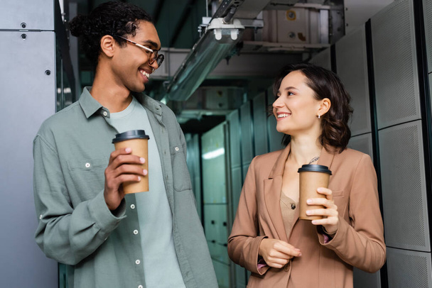 happy interracial programmers with paper cups talking in data center - Photo, Image