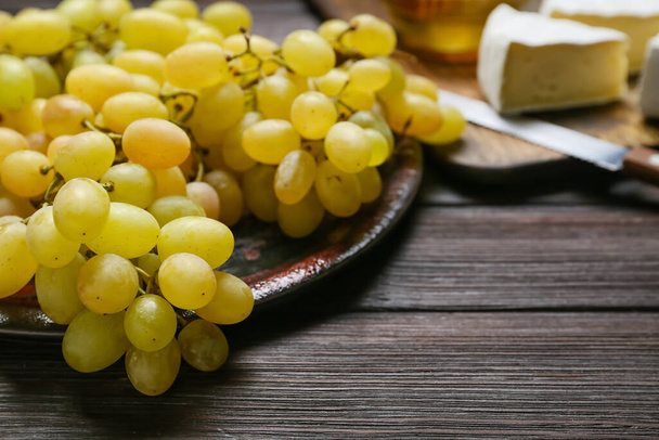Plate with ripe grapes on wooden background, closeup - 写真・画像