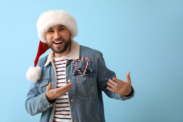 Knappe man in Santa hoed met snoep stokken op blauwe achtergrond - Foto, afbeelding