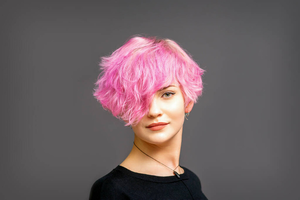 Retrato de una hermosa mujer blanca joven con un peinado corto rosa sobre fondo oscuro con espacio para copiar - Foto, imagen