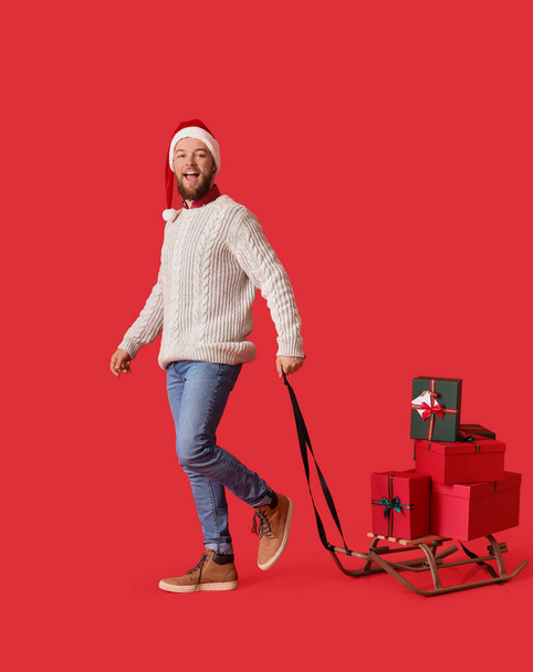 Going man with heap of Christmas gifts on sledges against color background - Zdjęcie, obraz