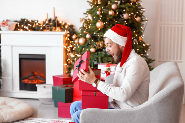 Hombre guapo abriendo regalos de Navidad en casa - Foto, imagen