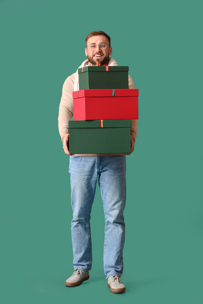 Schöner Mann mit Weihnachtsgeschenken auf farbigem Hintergrund - Foto, Bild
