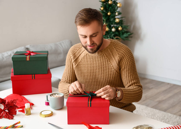 Komea mies pakkaamassa lahjoja kotona jouluaattona - Valokuva, kuva