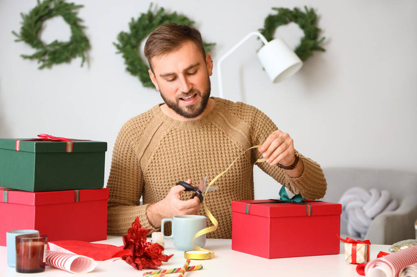 Красивый мужчина собирает подарки дома в канун Рождества - Фото, изображение