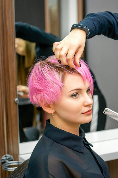 Kobieta fryzjer stylizacja krótkie różowe włosy młodej białej kobiety z rąk i grzebień w salonie fryzjerskim - Zdjęcie, obraz
