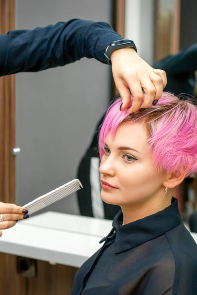 Женщина парикмахер укладка короткие розовые волосы молодой белой женщины с руками и расческа в парикмахерской - Фото, изображение
