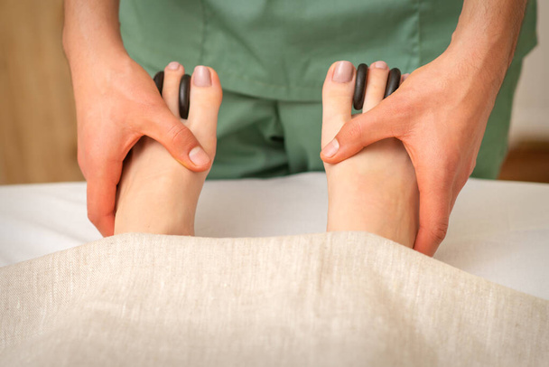 Massager doing feet and toes massage with rocks between a female toes - Foto, afbeelding