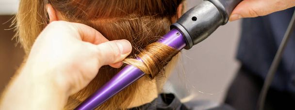 Close up de mãos de cabeleireiro usando um ferro de ondulação para cachos de cabelo em um salão de beleza - Foto, Imagem