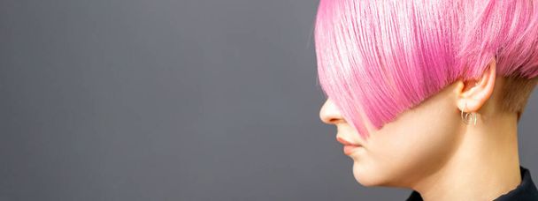 Retrato de perfil de una joven mujer caucásica con corte de pelo de color rosa bob aislado sobre un fondo gris, espacio para copiar - Foto, imagen