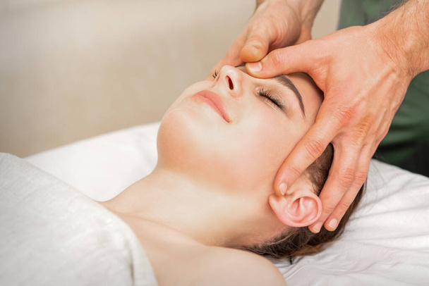 Jolie jeune femme caucasienne recevant un massage de la tête par un massothérapeute masculin dans un salon de beauté - Photo, image