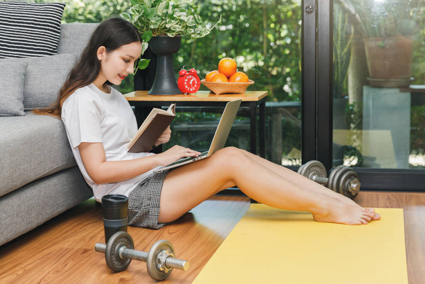 Schöne junge Frau sieht Fitness-Video-Tutorials online auf Laptop, während sie sich auf den Boden im Wohnzimmer setzt. - Foto, Bild