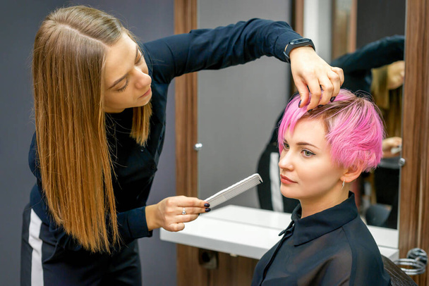 Cabeleireiro feminino styling cabelo rosa curto da jovem mulher branca com as mãos e pentear em um salão de cabeleireiro - Foto, Imagem