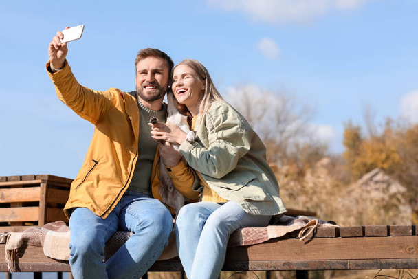 Lovely couple with cute dog taking selfie on autumn day - Фото, зображення