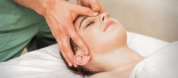 Pretty young caucasian woman receiving a head massage by a male massage therapist in a beauty salon - Zdjęcie, obraz