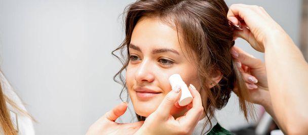 Makeup artist applying cream blush foundation tube on the cheek of the young caucasian woman in a beauty salon - Photo, image