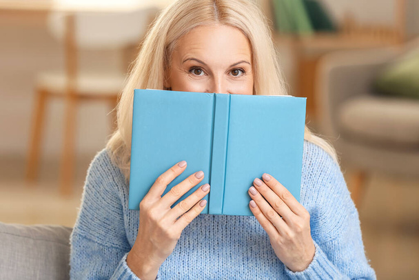 Hermosa mujer madura leyendo libro en casa en el día de otoño - Foto, imagen