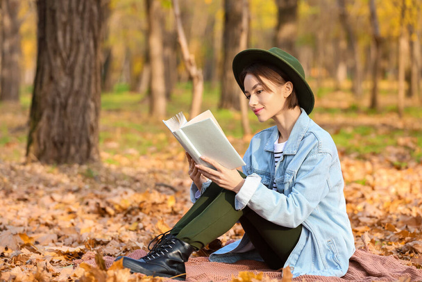 Młoda kobieta z ciekawą książką o kratę w jesiennym parku - Zdjęcie, obraz