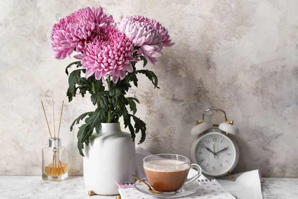 Vase with beautiful chrysanthemum flowers, cup of coffee and alarm clock on table - Foto, Imagen