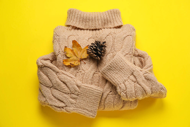 Warmer Pullover, trockenes Blatt und Tannenzapfen auf gelbem Hintergrund - Foto, Bild
