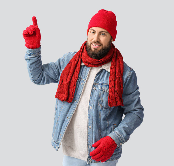 Hezký muž v zimním oblečení ukazuje na něco na světlém pozadí - Fotografie, Obrázek
