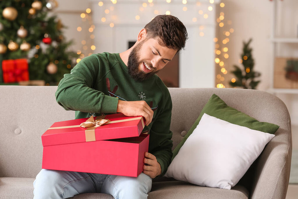 Onnellinen mies avaamassa joululahjaa kotona - Valokuva, kuva