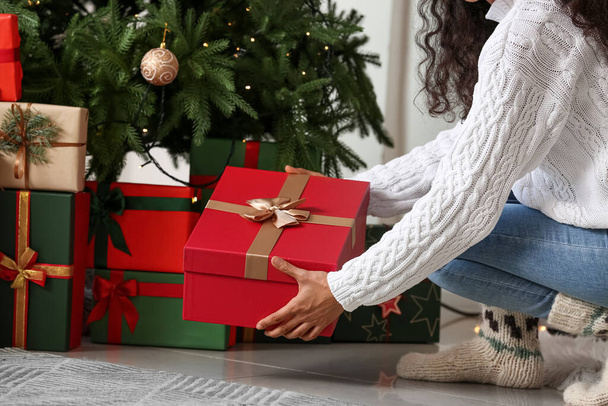 Frau legt Geschenk unter Weihnachtsbaum im Wohnzimmer - Foto, Bild