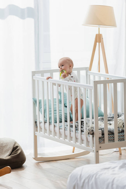 little boy standing in crib with toy near lamp - Foto, Bild