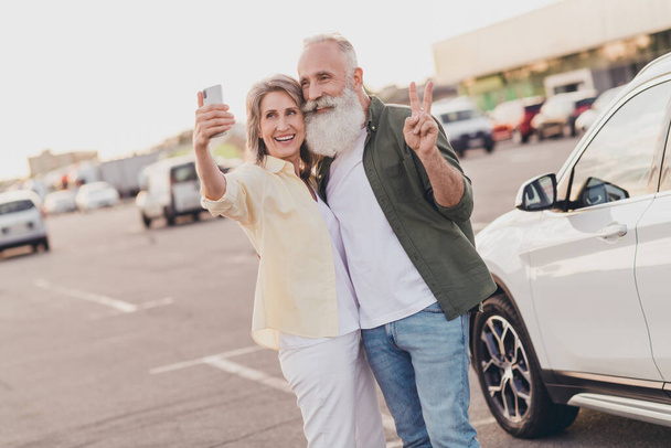 Photo of retired pensioner wife husband bearded grey haired old couple make selfie v-sign card park outside outdoors in urban city - Photo, image