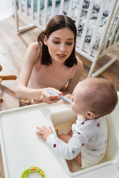 high angle view of brunette woman feeding blurred son in baby chair - Foto, Imagem
