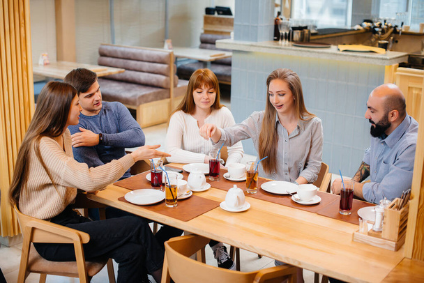 A group of young cheerful friends is sitting in a cafe talking and eating pizza. Lunch at the pizzeria. - Фото, изображение