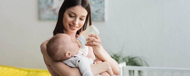 šťastná žena s kojeneckou láhev krmení malý syn doma, banner - Fotografie, Obrázek
