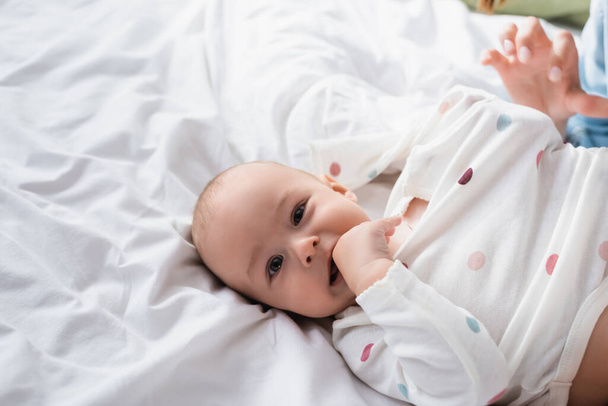 aus der Vogelperspektive: Baby hält Hand im Mund, während es auf dem Bett liegt - Foto, Bild