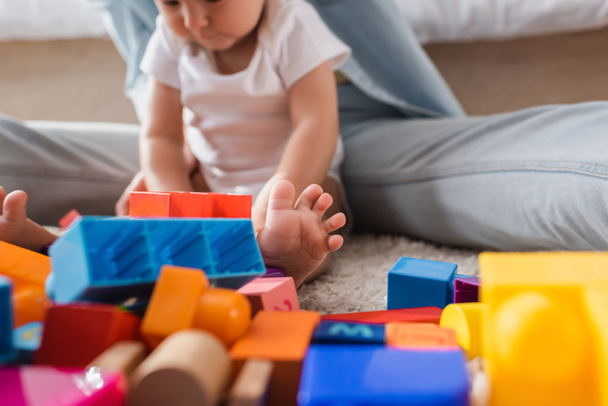 mujer borrosa y bebé niño jugando con bloques de construcción en el piso en casa - Foto, Imagen